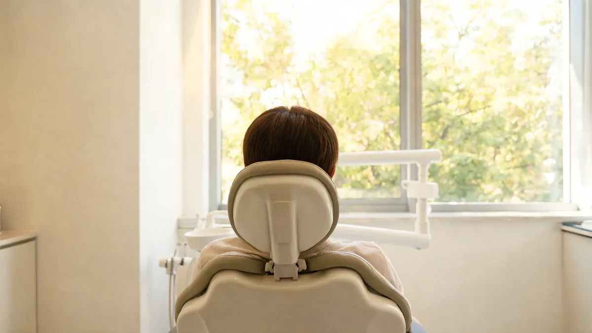 Patient seen from behind relaxing in a dental chair and looking out a large window in a bright treatment room